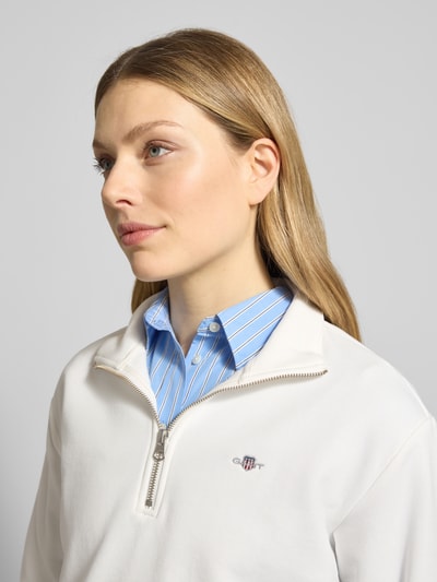 Modelka nosi Bluza 'Sweatshirt mit Baumwoll-Anteil' od Gant z mieszanki bawełny, luźny krój, kołnierz zapinany, wyhaftowane logo, prążkowane wykończenia. Zbliżenie na górną część ciała.