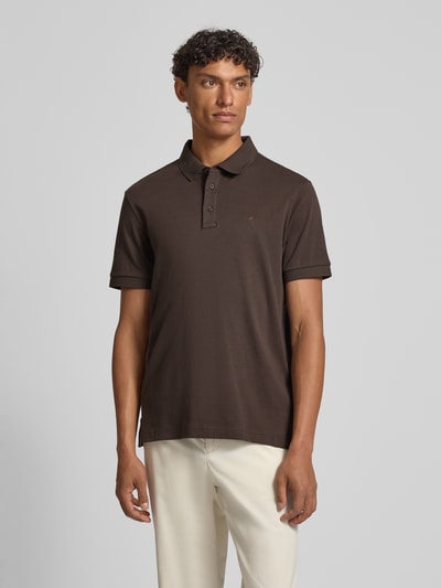 Männermodel trägt Modern Fit Poloshirt mit Logo-Stitching Modell 'Primo' von JOOP! Collection in Braun, reine Baumwolle, Ganzkörperansicht von vorne.
