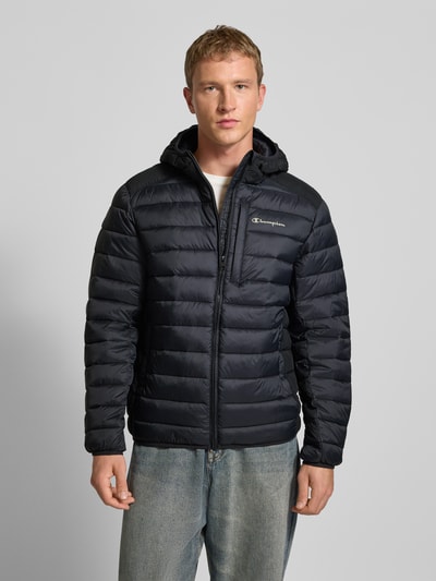 Männermodel trägt Steppjacke mit Kapuze und Logo von CHAMPION, Regular-Fit, Reißverschluss, Eingrifftaschen, Ganzkörperansicht von vorne.