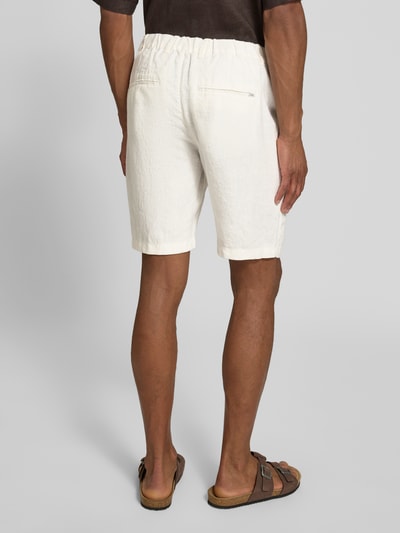 Mężczyzna nosi Leinen Shorts mit Eingrifftaschen Modell 'PANDRUP' od Casual Friday z czystego lnu, krój straight fit, białe, tylne kieszenie z lamówką, widoczne zapięcie na guzik i zamek, szerokość w rozmiarze M 44 cm, długość wewnętrzna nogawki 23 cm, widok całej sylwetki z tyłu.