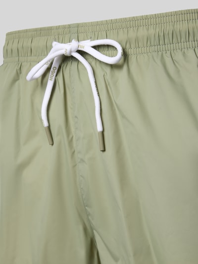 Produktfoto, Badeshorts mit Label-Print Modell 'HAITI' von HUGO, Optik: Unifarben, Tunnelzug, Bundabschluss: elastisch, seitliche Eingrifftaschen, Gesäßtasche, glatte Textur in hellem Grün.