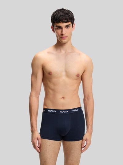 Männermodel trägt Slim Fit Trunks aus Baumwoll-Mix im 3er-Pack Modell 'PACK' von HUGO, Optik: Unifarben, Label-Schriftzug, Ganzkörperansicht von vorne.