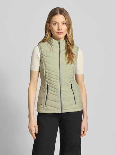 Frauenmodel trägt Steppweste mit 10.000 mm Wassersäule Modell 'GS109' von G.I.G.A. DX, Slim Fit, Stehkragen, Reißverschlusstaschen, helles Beige, glatte Struktur; Ganzkörperansicht von vorne. Rückenlänge 61 cm, Schulterbreite 37 cm, Brustweite 49 cm bei Größe 36.