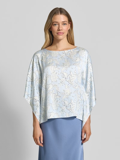 Kobiece model nosi Loose Fit Poncho-Bluse mit Allover-Muster od s.Oliver BLACK LABEL, efekt: wzór na całej powierzchni, krój loose fit, dekolt w łódkę, rękawy nietoperzowe, wykończenie materiału: tkanina, materiał: czysta wiskoza, jasnoniebieska z białym wzorem, gładka tekstura, całkowity widok z przodu.