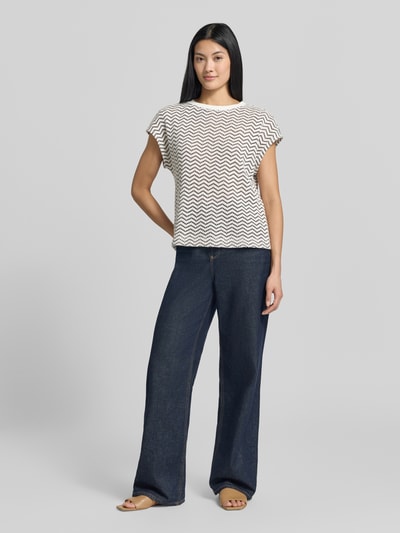 Modelka nosi Regular Fit T-Shirt in Strick-Optik od COMMA, mieszanka bawełny, półprzezroczysty materiał, krótki rękaw, dekolt w łódkę, długość tyłu w rozmiarze 36 to 53 cm, jasny i ciemnoniebieski, imitacja dzianiny, zygzakowaty wzór, Ganzkörperansicht von vorne.