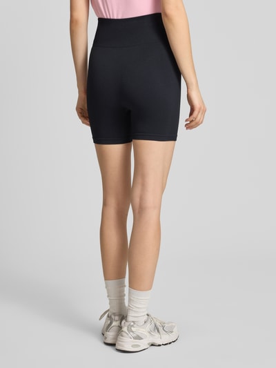 Frauenmodel trägt Slim Fit Shorts mit Logo-Print Modell 'Restore' von P.E Nation in Schwarz, Elastischer-Material-Mix, breiter Bund, Ganzkörperansicht Rückansicht.