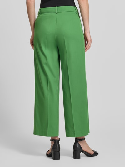 Frauenmodel trägt Wide Leg Hose aus Viskose-Mix mit Bügelfalten von More & More in Grün, Stoff leicht, Ganzkörperansicht Rückansicht. Damen Hose mit Baumwoll-Anteil, Knopf- und Reißverschluss, Bundweite 39 cm, Innenbeinlänge 66 cm.