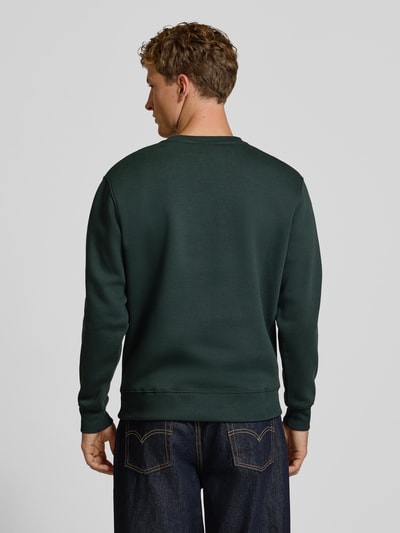 Männermodel trägt Regular Fit Sweatshirt aus Baumwoll-Mix mit Logo-Print von Alpha Industries in Dunkelgrün, Rückenansicht, Ganzkörperansicht Rückansicht. Baumwoll-Mix, gerippte Abschlüsse, Langarm, Rundhalsausschnitt, Rückenlänge 67 cm, Ärmellänge 64 cm.