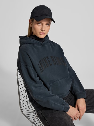 Frauenmodel trägt Oversized Hoodie mit Logo-Stitching von Anine Bing in dunklem Blau aus reiner Baumwolle, Oversized-Fit, Känguru-Tasche, elastische Abschlüsse, Rückenlänge bei Größe S 63 cm, Nahaufnahme Oberkörper.