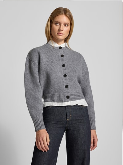 Vrouwenmodel draagt grijze gebreid jack van Knit Cardigan aus Wolle van Style Icon Collection, puur katoen, los model, doorlopende knoopsluiting, ribboorden, ruglengte maat S 46 cm, mouwlengte maat S 58 cm. Ganzkörperansicht van voren.