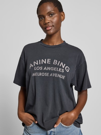 Frauenmodel trägt Relaxed Fit T-Shirt mit Logo-Print von Anine Bing aus Reiner Baumwolle, dunkle Farbe, Rundhalsausschnitt, Ganzkörperansicht von vorne.