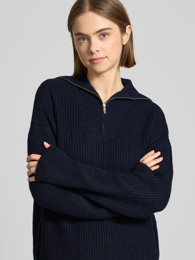 Vrouwenmodel draagt een donkerblauwe Strickpullover mit Reißverschluss Modell 'Kylie' van LeGer by Lena Gercke, grof gebreid, relaxed fit, materiaal-mix met wol, detailopname bovenlichaam.