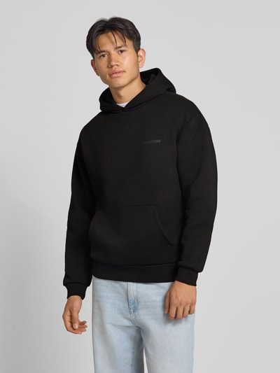 Männermodel trägt schwarzes Relaxed Fit Sweatshirt aus Baumwoll-Mix von REVIEW mit Känguru-Tasche, Ganzkörperansicht von vorne.