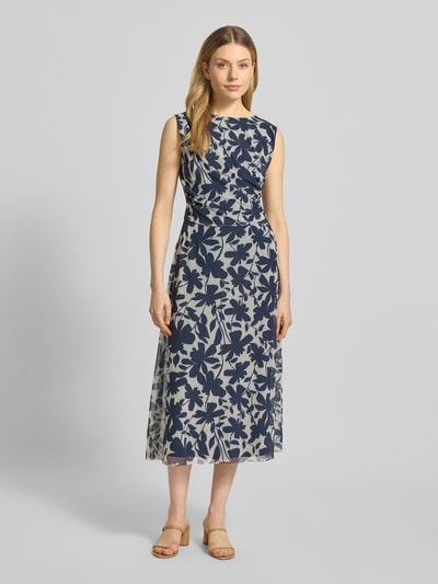 Modelka kobieca ma na sobie Regular Fit Midikleid mit floralem Allover-Print od Swing, granatowy florystyczny wzór na beżowym tle, krój regular fit, okrągły dekolt, bez rękawów, elastyczna tkanina z podszewką, marszczenia i zamek. Szerokość w rozmiarze 36: 47 cm, długość tyłu: 126 cm. Widok całej sylwetki z przodu.
