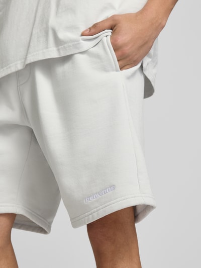 Männermodel trägt Shorts mit elastischem Bund und Logo-Stitching von Pegador aus Baumwoll-Mix in Weiß, Loose-Fit, Nahaufnahme Oberschenkel.