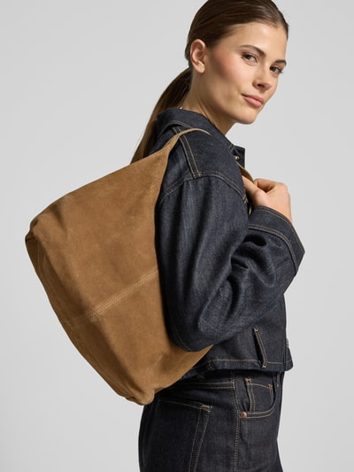 Frauenmodel trägt Handtasche aus Leder mit Schulterriemen von Mango in Braun, kombiniert mit dunkler Jeansjacke, Nahaufnahme Oberkörper. Echtes Leder, Hauptfach mit Reißverschluss, Schulterriemen 44 cm, Maße 28x22x16 cm.