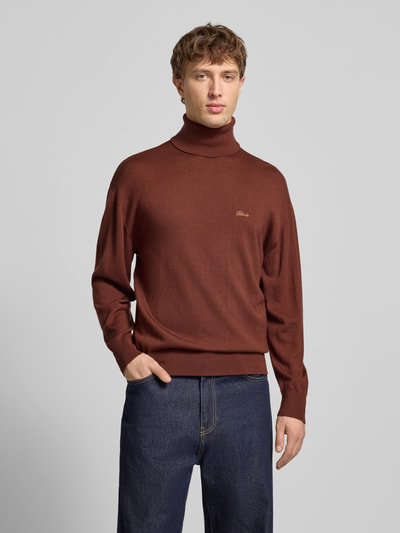 Männermodel trägt Loose Fit Rollkragenpullover aus Woll-Mix von BLKVIS in Braun mit gerippten Abschlüssen und Label-Stitching, Nahaufnahme Oberkörper. Rückenlänge bei Größe M: 68 cm, Ärmellänge 57 cm.