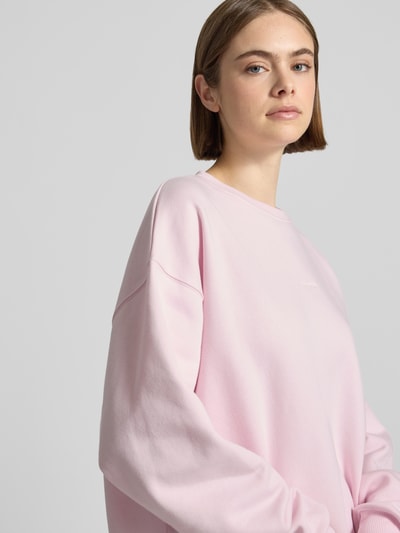 Frauenmodel trägt Oversized Sweatshirt mit Logo-Print von OH APRIL in zartem Rosa aus Baumwoll-Mix, Nahaufnahme Oberkörper.
