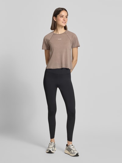 Frauenmodel trägt Cropped Fit T-Shirt mit Logo-Print von Salomon in Braun, rundhals, kurzärmelig, Ganzkörperansicht von vorne.
