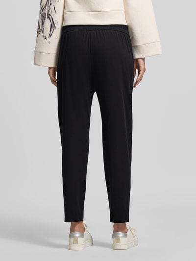 Frauenmodel trägt Hose mit elastischem Bund und Eingrifftaschen von Marc Cain in Schwarz, Material-Mix, Regular Fit, Ganzkörperansicht Rückansicht.