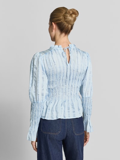Frauenmodel trägt Bluse in tailliertem Schnitt mit Smok-Details Modell 'RAVA' von YAS, hellblau mit feiner Struktur, Ganzkörperansicht Rückansicht. Viskose-Mix mit Lyocell-Anteil, Rückenlänge 54 cm, Ärmellänge 65 cm.