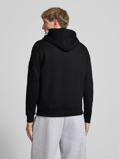 Männermodel trägt Regular Fit Hoodie aus Baumwoll-Mix mit Label-Patch von Alpha Industries, Schwarz, Ärmel-Tasche, Rückenansicht.