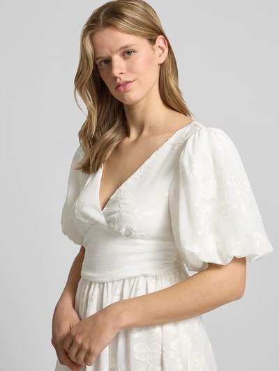 Frauenmodel trägt Minikleid mit Ballonärmeln von Gina Tricot, tailliert, V-Ausschnitt, Embroidery Design, weiß, Nahaufnahme Oberkörper.