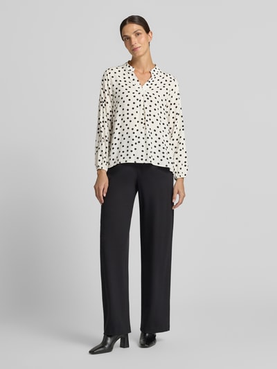 Frauenmodel trägt Relaxed Fit Bluse aus reiner Viskose-Mix Modell 'Valeria' von ZABAIONE, weiß mit schwarzen Punkten, Ganzkörperansicht von vorne. Damen Bluse, Serafino Ausschnitt, langärmelig, Rückenlänge 54 cm, Ärmellänge 58 cm.