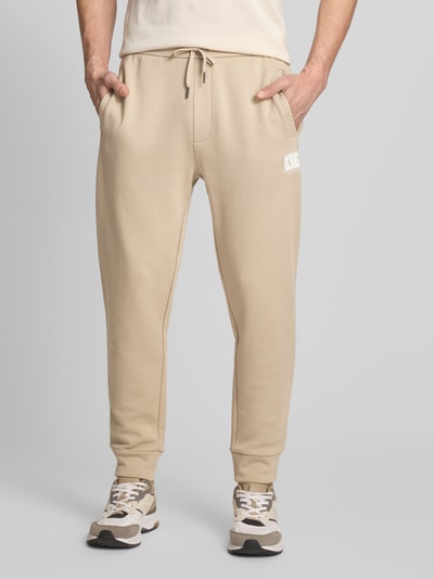Männermodel trägt Regular Fit Sweatpants aus reiner Baumwolle von ARMANI EXCHANGE in Beige mit Label-Print, Kordelzug, Seitentaschen, Ganzkörperansicht von vorne.