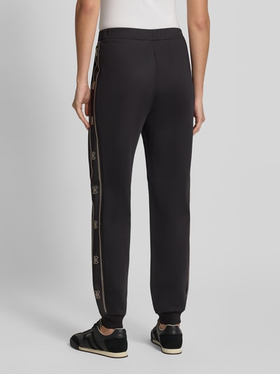 Frauenmodel trägt Sweatpants mit Label-Detail Modell 'OCTAVIA' von GUESS, Regular Fit, Schwarz, elastischer Bund, Ganzkörperansicht Rückansicht.