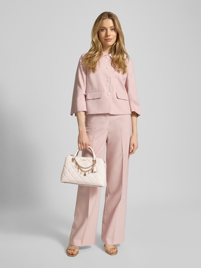 Kobiece model prezentuje torebkę w stylu skóropodobnym, model 'Libby' od Guess, z efektem pikowania, zapięciem na magnes, uchwytem i odpinanym paskiem na ramię, kieszenią zapinaną na zamek błyskawiczny, detalami z logo i ozdobnym obszyciem, szerokość w rozmiarze 1: 32 cm, długość: 21 cm, głębokość: 11 cm, długość paska na ramię: 122 cm, widok całej sylwetki z przodu.