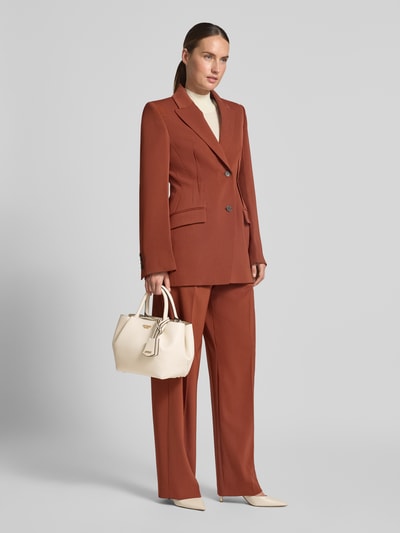 Frauenmodel trägt Handtasche in Leder-Optik Modell 'Amorette' von GUESS, beige Farbe, Logo-Detail, Nahaufnahme Oberkörper, geteilter Hauptfach, Magnetverschluss, abnehmbarer Trageriemen, strukturierte Oberfläche, Maße: 28x23x15 cm, Länge Schulterriemen: 118 cm. Ganzkörperansicht von vorne.