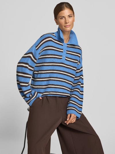 Frauenmodel trägt Pullover mit Woll-Anteil und kurzer Knopfleiste von Smith and Soul, blau-weiß gestreift, Loose Fit, Polokragen, überschnittene Schultern, braune Hose, Nahaufnahme Oberkörper.