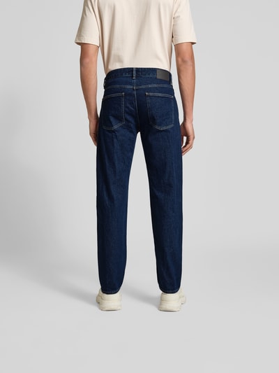 Männermodel trägt Straight Fit Jeans mit Logo-Patch von Closed aus dunklem Baumwoll-Mix, 5-Pocket-Design, Rückansicht Ganzkörperansicht.