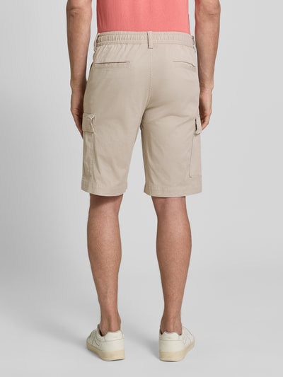 Männermodel trägt Relaxed Fit Cargoshorts aus Baumwoll-Mix Modell 'SISLA' von BOSS Orange in Beige mit Cargotaschen, Ganzkörperansicht Rückansicht.