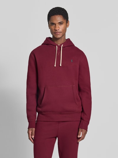 Männermodel trägt Regular Fit Hoodie aus Baumwoll-Mix von Polo Ralph Lauren in Dunkelrot mit Kängurutasche und beigem Kordelzug, Ganzkörperansicht von vorne. Herren Hoodie von Polo Ralph Lauren