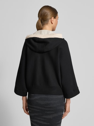 Vrouwenmodel draagt Strickjacke mit Reißverschluss van Marc Cain, zwart, losse pasvorm, capuchon, ribboorden, 3/4-mouw, rugaanzicht.