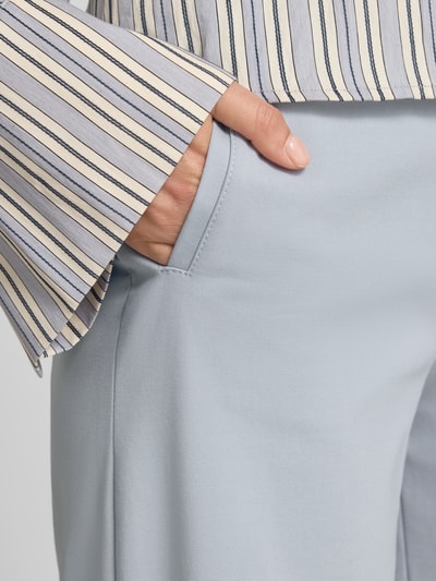 Kobieta nosi spodnie materiałowe model 'FAE' od Drykorn z mieszanki bawełny z dodatkiem streczu, wpuszczane kieszenie, krój wide leg fit, jasnoniebieski kolor, długość wewnętrzna nogawki 82 cm w rozmiarze 27/34, szerokość w rozmiarze 27/34: 37 cm, zapięcie na haftkę i zamek błyskawiczny, z tyłu kieszeń z wypustką, detailaufnahme wpuszczanej kieszeni.