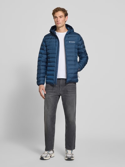 Męskamodel nosi kurtkę pikowaną Regular Fit Model 'Lake 22™' od Columbia z kapturem, nadrukiem z logo, zamkiem błyskawicznym, kolor niebieski, Długość tyłu w rozmiarze M: 72 cm, Szerokość ramion w rozmiarze M: 43 cm, Szerokość klatki piersiowej w rozmiarze M: 42 cm, Długość rękawów w rozmiarze M: 70 cm, Ganzkörperansicht von vorne.