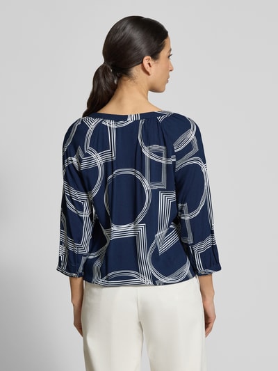 Vrouwenmodel draagt Relaxed Fit Bluse uit pure viscose model 'Cornelia' van ZABAIONE, marineblauw met witte grafische vormen, 3/4-mouw, tuniekhals, gezette mouwuiteinden, elastische zoom, ruglengte 65 cm, mouwlengte 29 cm, complete achteraanzicht.