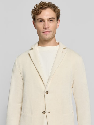 Männermodel trägt Regular Fit Cardigan mit woll-anteil van Manuel Ritz, materiaalmix, reverskraag, tricotlook, opgestikte zakken, ecru, nahaufnahme bovenlichaam.