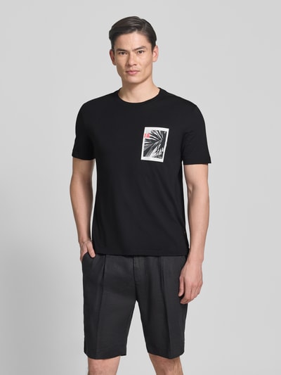 Männermodel trägt Regular Fit T-Shirt aus reiner Baumwolle Modell 'TE_BOARD' von BOSS Orange, unifarben schwarz, Foto-Print, Ganzkörperansicht von vorne.