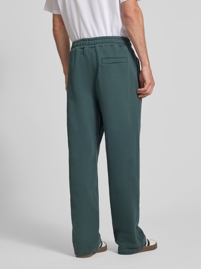 Männermodel trägt Loose Fit Sweatpants aus Baumwoll-Mix mit Label-Detail von PEGADOR, grün, elastischer Bund, Rückansicht, Ganzkörperansicht.