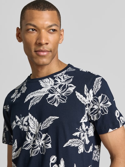Männermodel trägt T-Shirt mit Rundhalsausschnitt und Label-Detail von Lerros, reine Baumwolle, navy mit weißem Blumenmuster, Nahaufnahme Oberkörper.