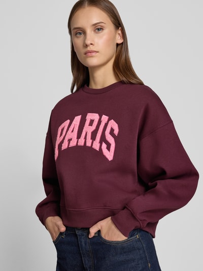 Vrouwenmodel draagt relaxed fit dames sweatshirt van katoenmix Model 'Tatum' van JJXX, bordeaux met roze statementpatch, ronde hals, ribboordjes, met lange mouwen, overgesneden schouders, Ganzkörperansicht van voren.