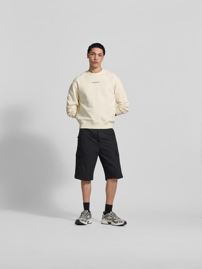 Männermodel trägt Hoodie aus Baumwoll-Mix von MAISON KITSUNÉ in Creme, lockere Passform, elastische Abschlüsse, Ganzkörperansicht von vorne.