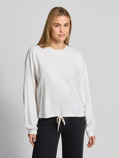 Frauenmodel trägt Relaxed Fit Langarmshirt aus reine Baumwolle von DRYKORN, weiß, gerippte Blende und Bündchen, Ganzkörperansicht von vorne.