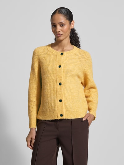 Modelka kobieca nosi Regular Fit Strickjacke aus Woll-Mix mit Alpaka-Anteil Modell 'LULU' od Selected Femme, żółty, krój regular fit, raglanowe rękawy, długi rękaw, zapięcie na guziki, dekolt typu crew neck, faktura prążkowana, zdjęcie całej sylwetki z przodu.