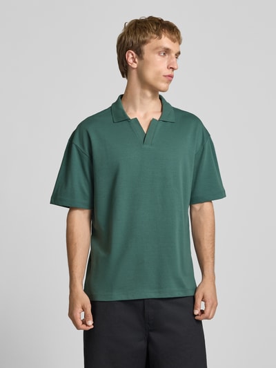 Mężczyzna nosi Boxy Fit Poloshirt aus Baumwoll-Mix Modell 'CASPIAN AIRLEX' od Only & Sons, jednolity kolor, krój boxy fit, jersey, naszywka z logo, krótki rękaw, polowy kołnierz, przód, zdjęcie całej sylwetki z przodu.