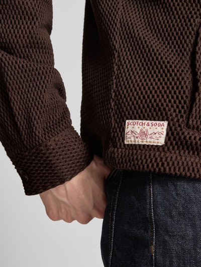 Mężczyzna nosi Regular Fit Hemdjacke mit Strukturmuster od Scotch & Soda, brązowa bawełna, krój regular fit, tekstura, detal rękawa, zbliżenie na dolną część ręki